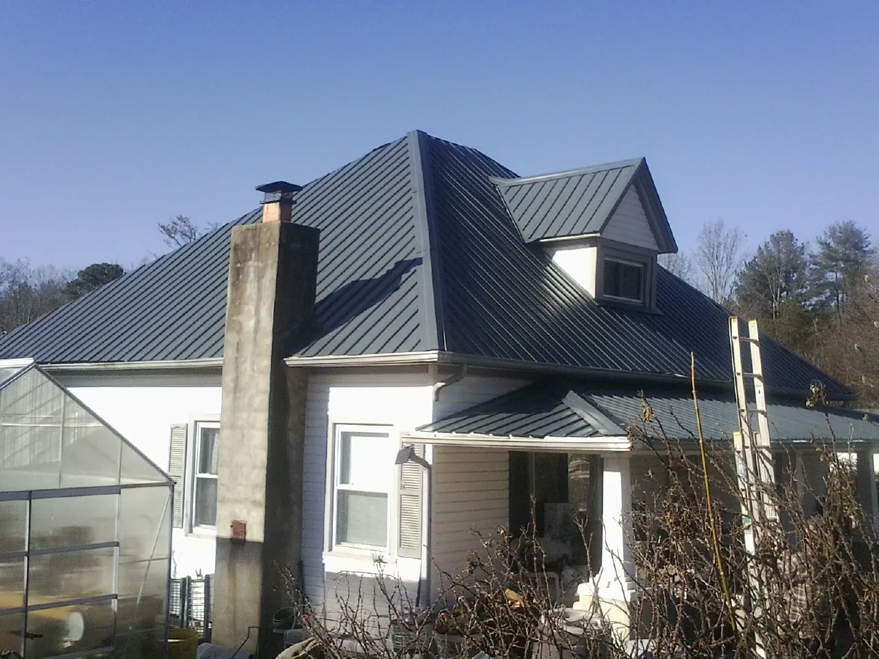 Dark blue standing seam metal roof on a white farmhouse with dormer — Slate & Tile Roof Repair by Roofing Brothers in Crawford