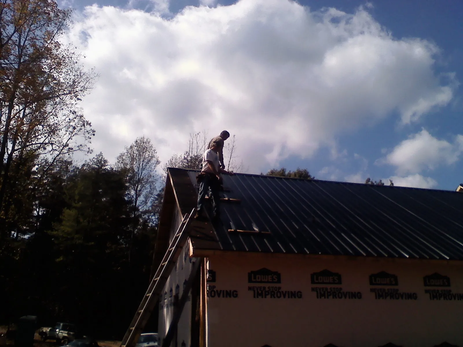 Roofer fastening dark metal panels high against a cloudy sky, from a Roof Inspection job in Crawford